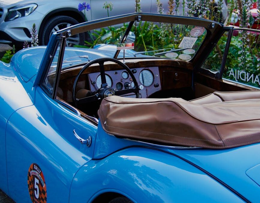 Triumph bleu classique garé à l'extérieur avec un environnement floral, présentant un design élégant.