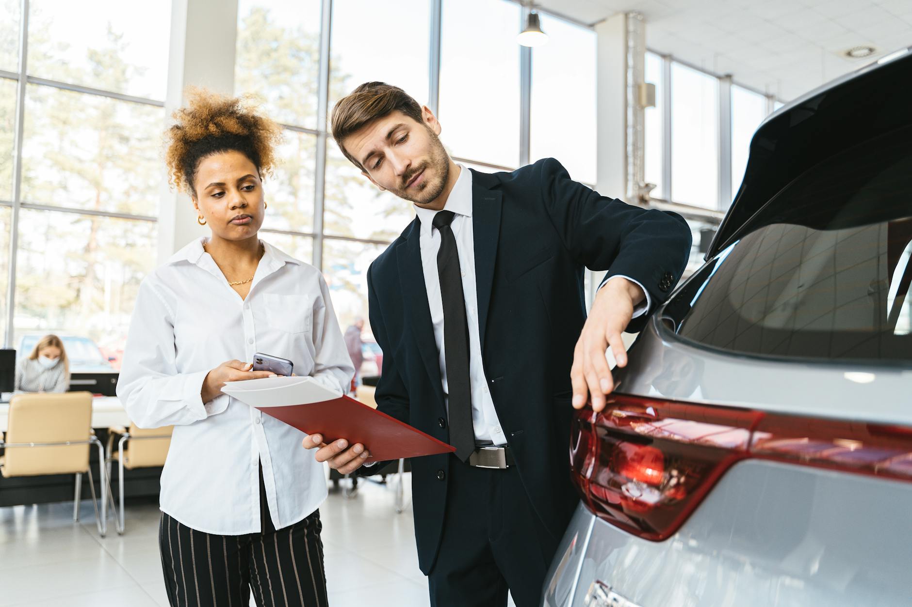 Homme d'affaires et client discutant de l'achat d'une voiture dans une salle d'exposition moderne.